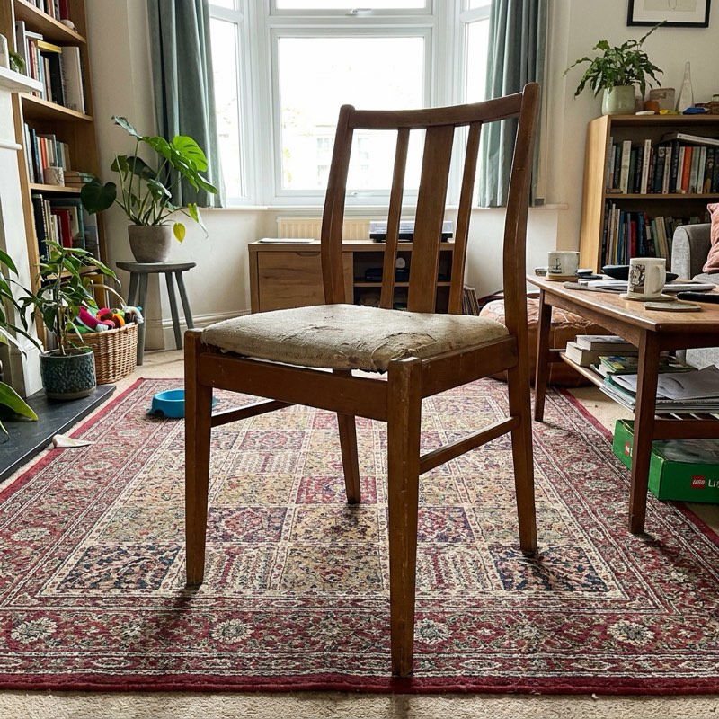 A mid-century wooden dining chair on a rug.